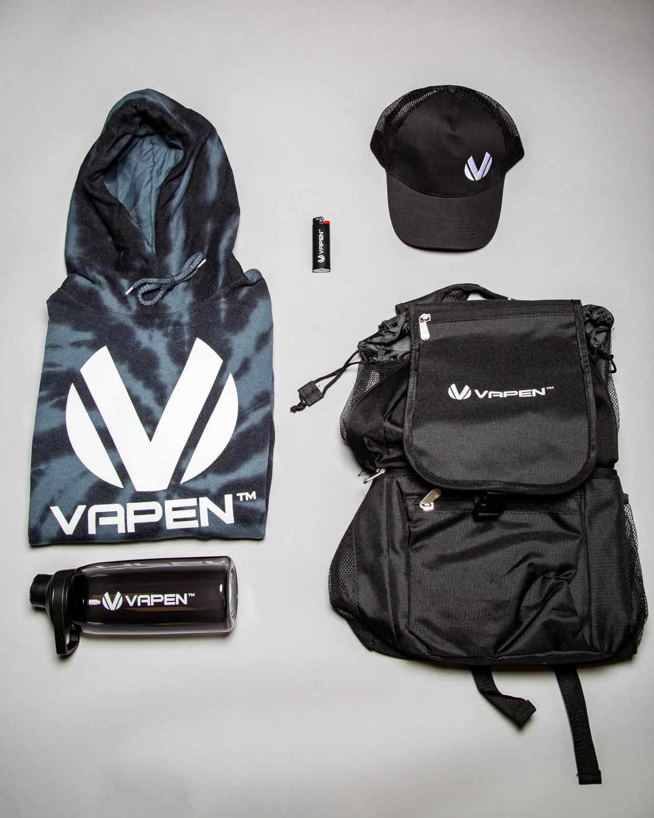 Flat lay of Vapen merch: hoodie, cap, lighter, water bottle and backpack