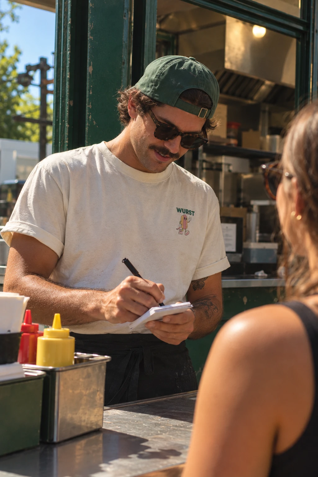 Wurst cook in a green cap and Wurst tee taking an order at the stand window