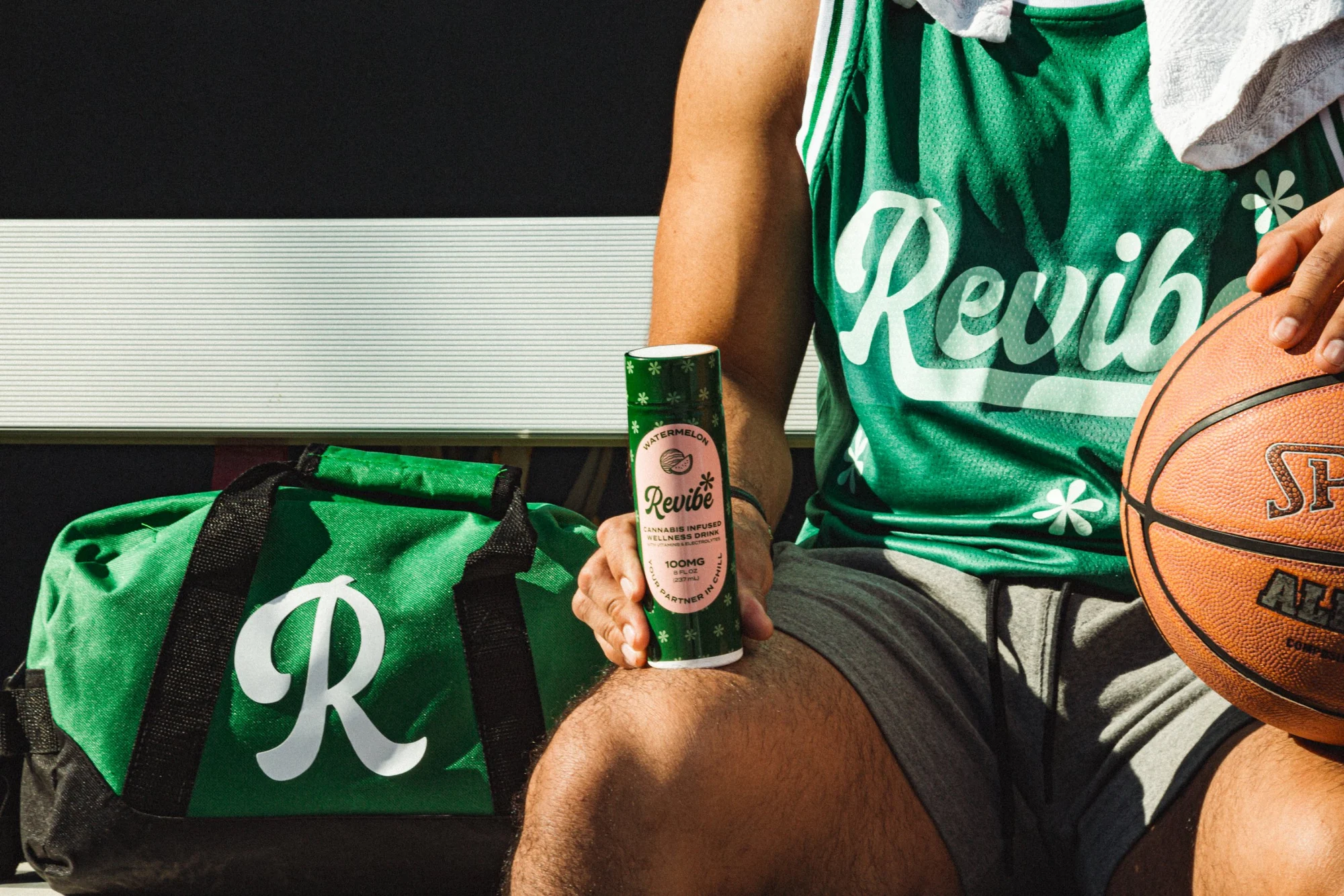 Revibe watermelon drink on a knee beside an R duffel bag and basketball