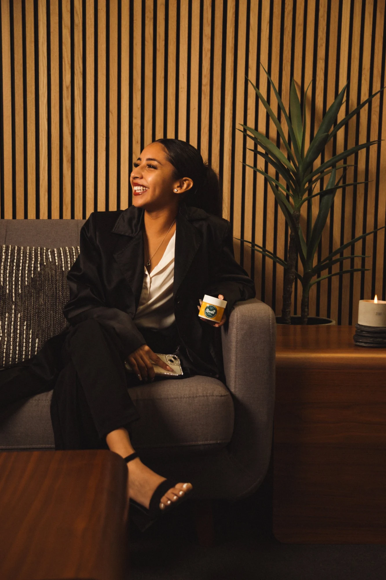 Woman laughing on a couch holding a Revibe gummy jar