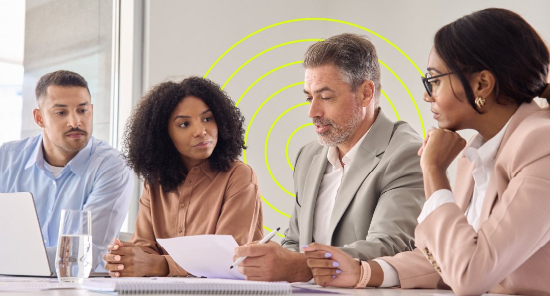 Four colleagues reviewing papers at a table, yellow circles behind them