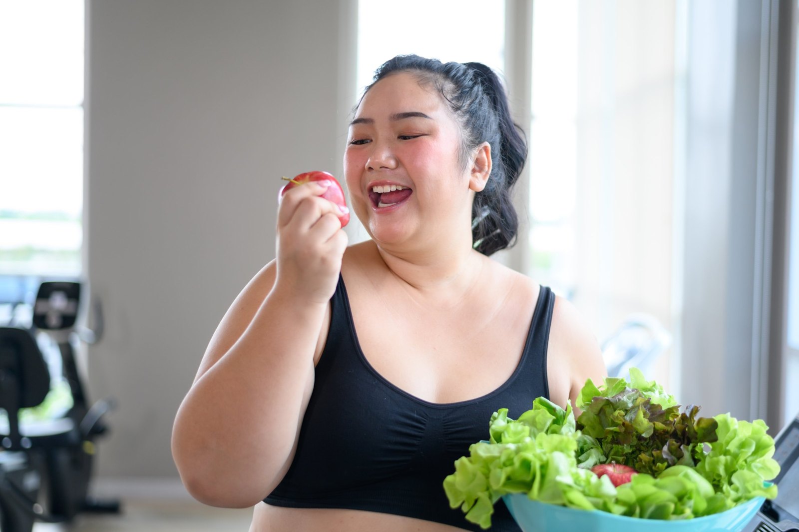Smiling woman holding an apple next to a bowl of greens